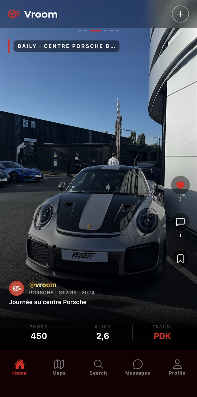 Une Porsche GT2 RS grise photographiée devant un centre Porsche, avec sa puissance, son 0 à 100 et sa transmission affichés en bas de l'écran.